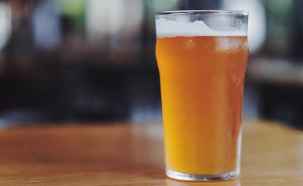 Pint of west coast IPA beer with a foamy head on a wooden bar table