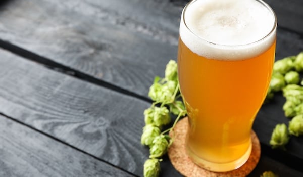 Glass of pale ale beer and hop cones on wooden background.